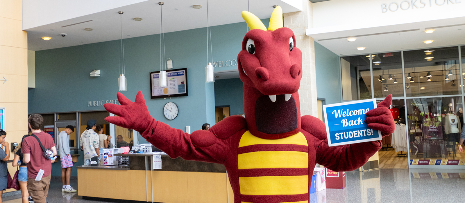 Howard Community College’s dragon mascot welcomes students back in the Rouse Company Foundation Student Services Hall, holding a sign that says ‘Welcome Back Students!’ near the bookstore and Welcome Center.