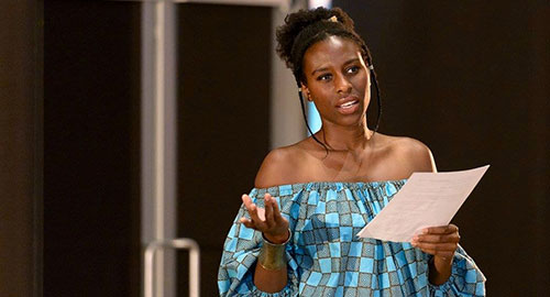 Speaker onstage holding a sheet of paper and gesturing while addressing the audience
