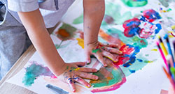 the hands of a children finger painting on paper