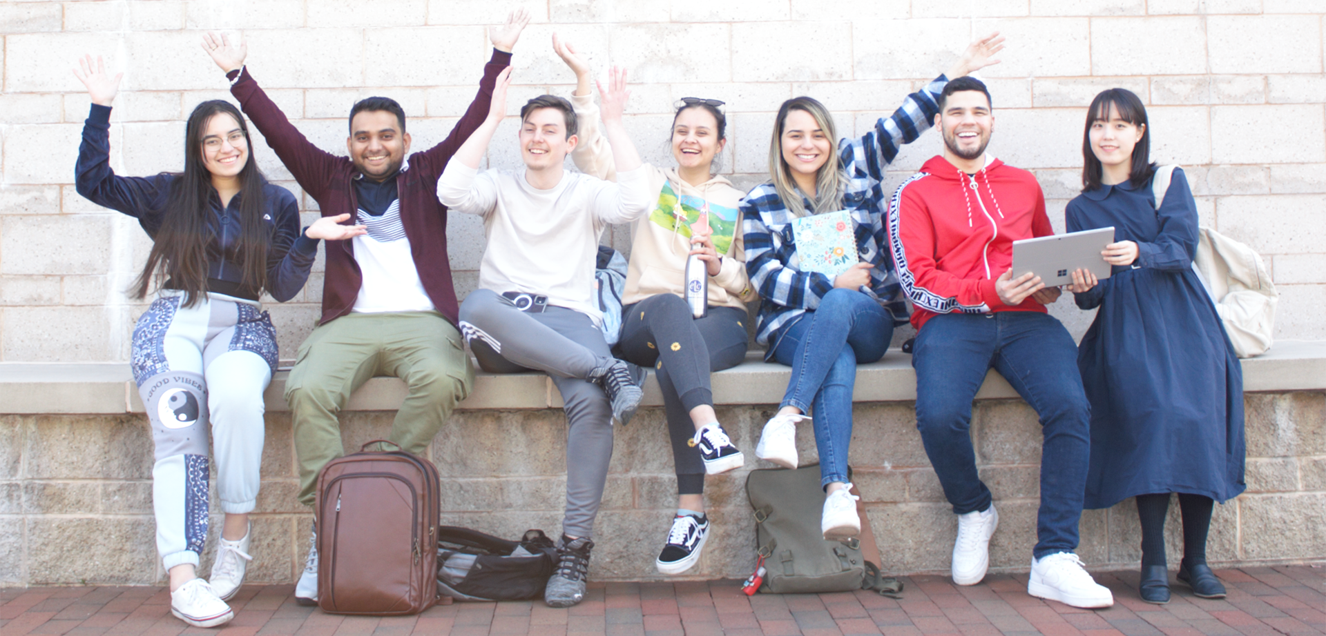 Group of students sitting in the Quad with their arms raised up