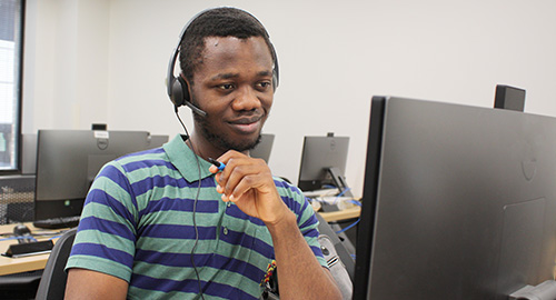 A young black man at a computer with headphones on