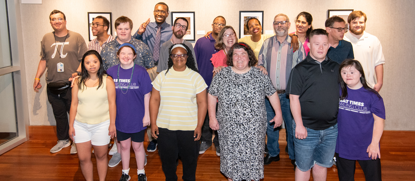 A group of smiling adults posing together in the HCC art gallery, celebrating friendship and inclusion.