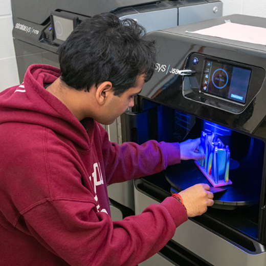 A student kneeling in front of a 3d printer to make a model