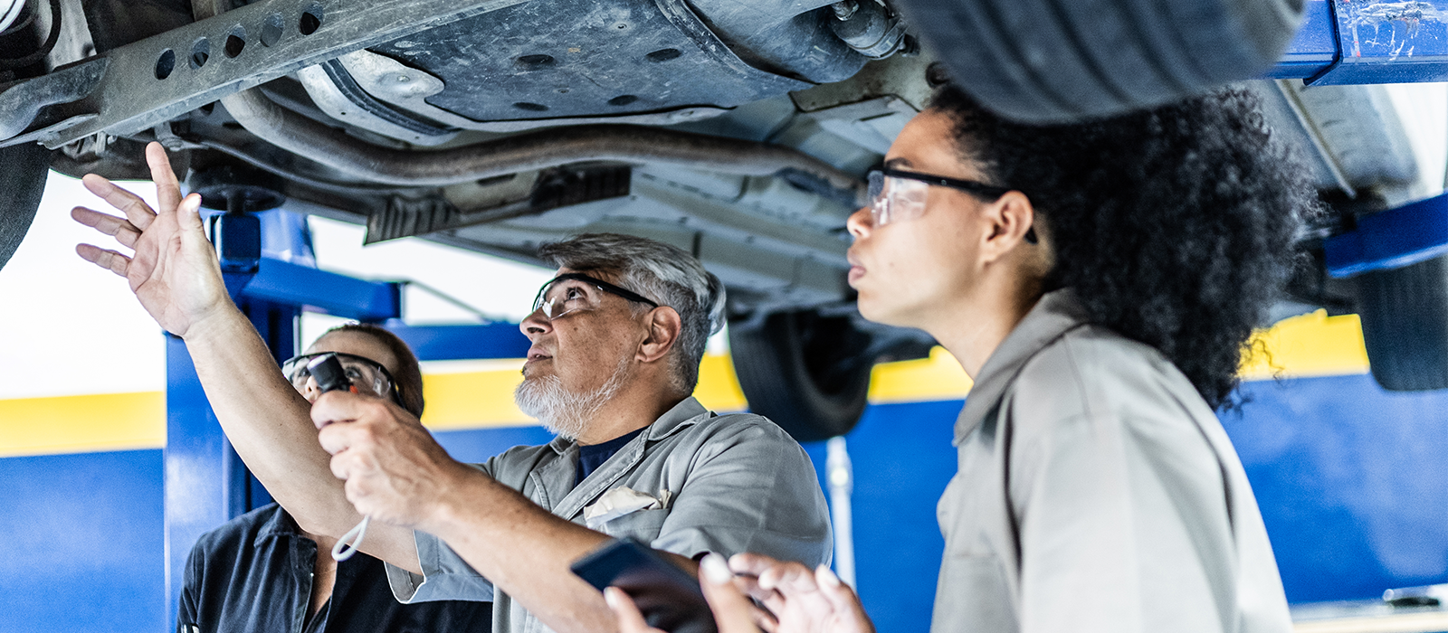 A man and woman inspect a vehicle beneath a car lift in an automotive workshop.