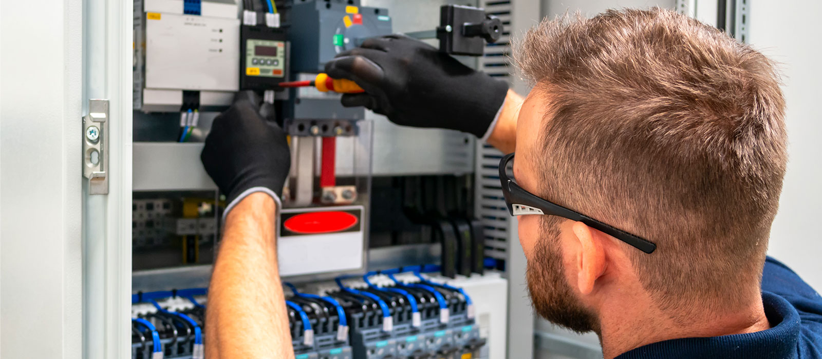 A man working with an electronics tool in a network switch closet