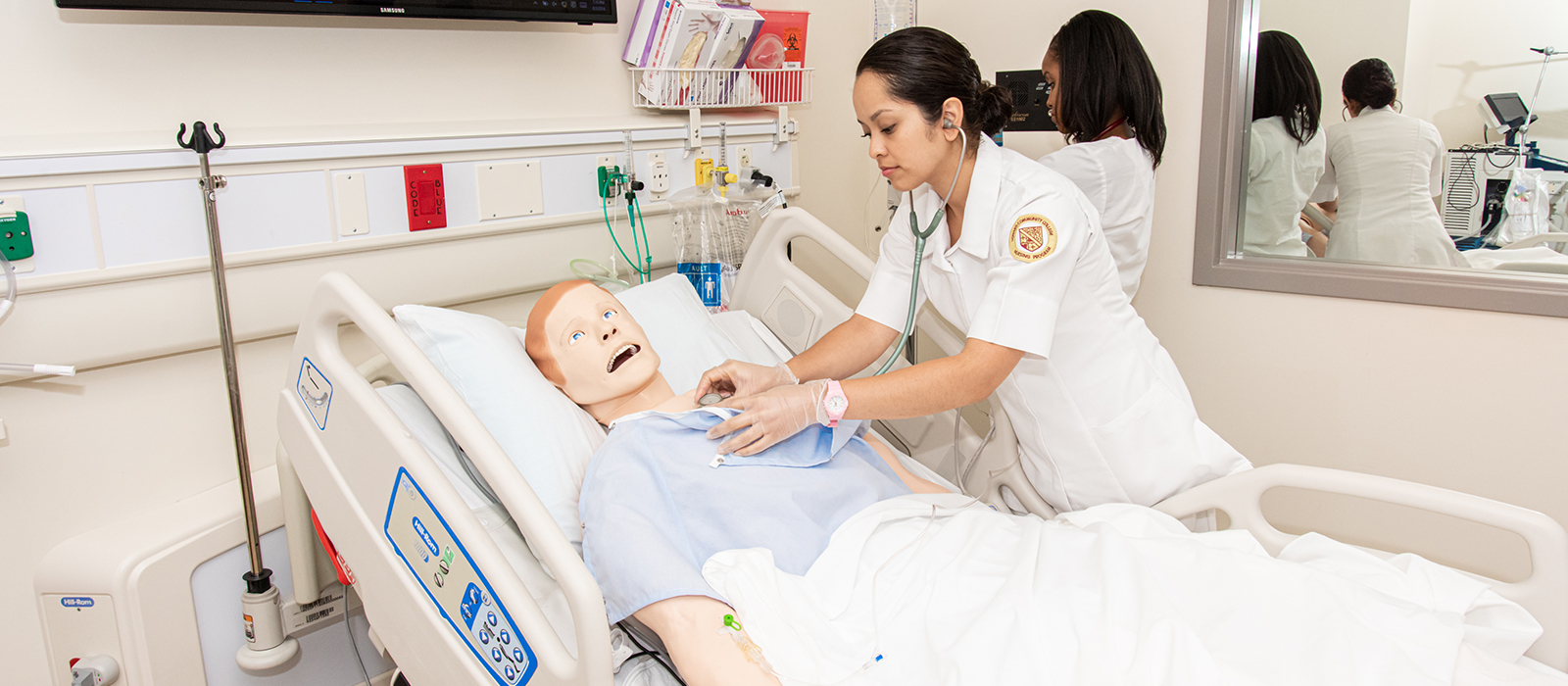 A nursing student using a stethoscope to check the heart of a dummy lying in a hospital bed