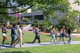 A diverse group of smiling students walk through the Quad at Howard Community College, holding papers and folders during what appears to be a new student orientation event